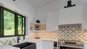 A modern kitchen with white cabinetry, a built-in oven, and a window with a view of greenery.