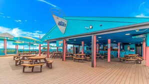 Een terras met picknicktafels en parasols, een bar en een bord met de tekst 'The Quarter Deck'.