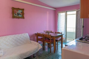 Ein Zimmer mit pinkfarbener Wand, einem weißen Sofa, einem Holzespeisetisch mit Stühlen und einer Küchenzeile mit Gasherd.
