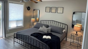 A bedroom with a bed, ceiling fan, bedside lamps, a clock, and framed artwork. - Luxurious Waterfront Retreat on Paudash Lake - Ridgestone Cottage (Highlands East)