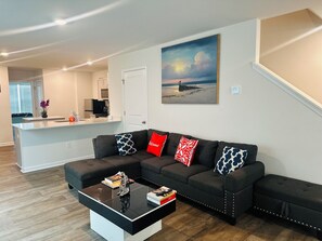 Una sala de estar moderna con un sofá oscuro, una mesa de centro y un cuadro con una escena de playa.