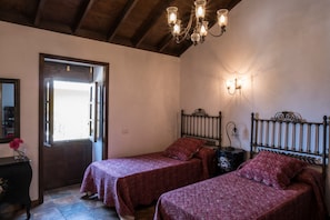 Une chambre avec deux lits, un plafond en bois, un lustre et une porte donnant sur l’extérieur.