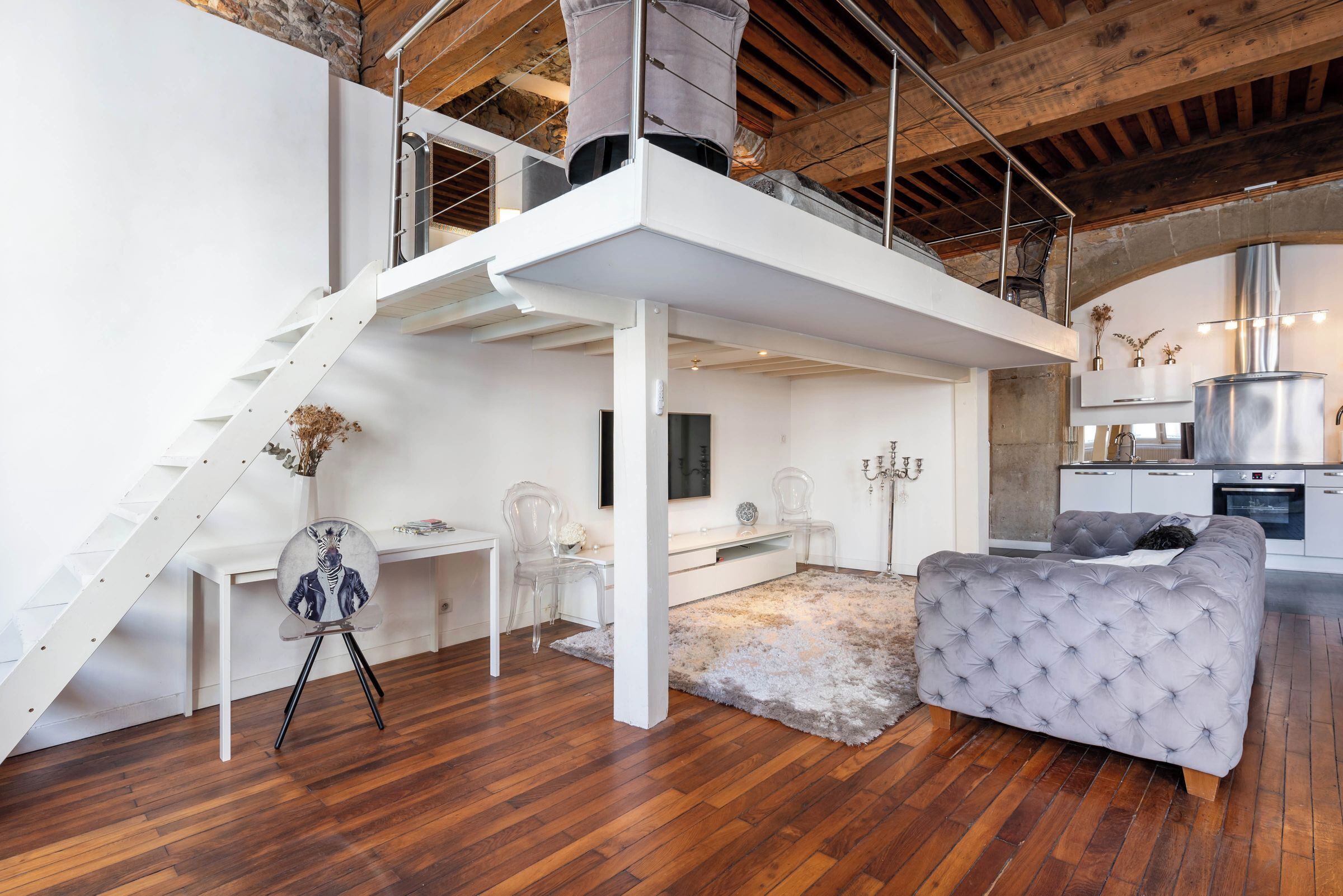 A modern loft-style room with a staircase, a dining area, a sofa, and a kitchen area.