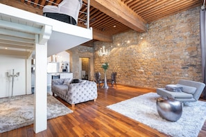 Ein Loft-Wohnraum mit Steinwand, Holzbalken, Essbereich und einer Couch.