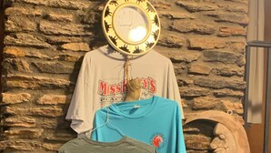 Eine Steinsäule mit einer Uhr und zwei auf einem Gestell hängenden T-Shirts.