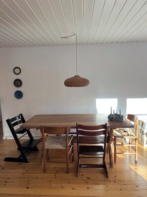 Un coin repas avec une table et des chaises en bois, un luminaire suspendu et des assiettes décoratives fixées au mur.