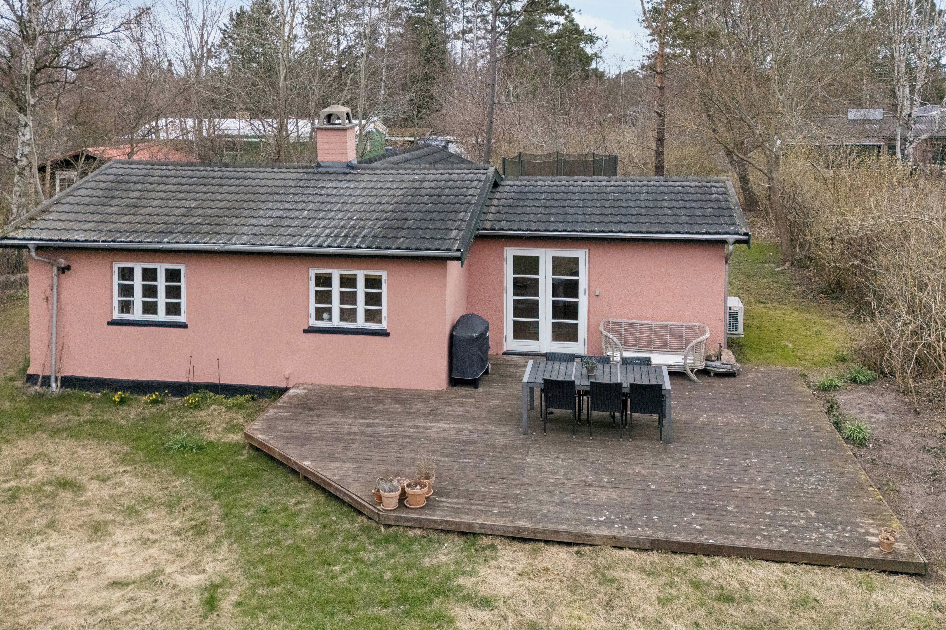 A pink house with a wooden deck, a covered grill, and a patio table.