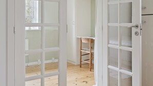 Eine geöffnete Tür, die einen Raum mit Holzboden, einem Stuhl und einem weißen Schrank mit Schubladen zeigt.