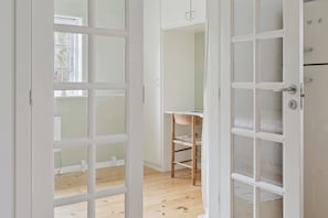 Eine geöffnete Tür, die einen Raum mit Holzboden, einem Stuhl und einem weißen Schrank mit Schubladen zeigt.