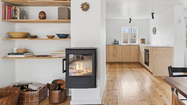 Eine moderne Küche mit Kaminofen, Holzregalen mit Keramik und Blick in den Essbereich.