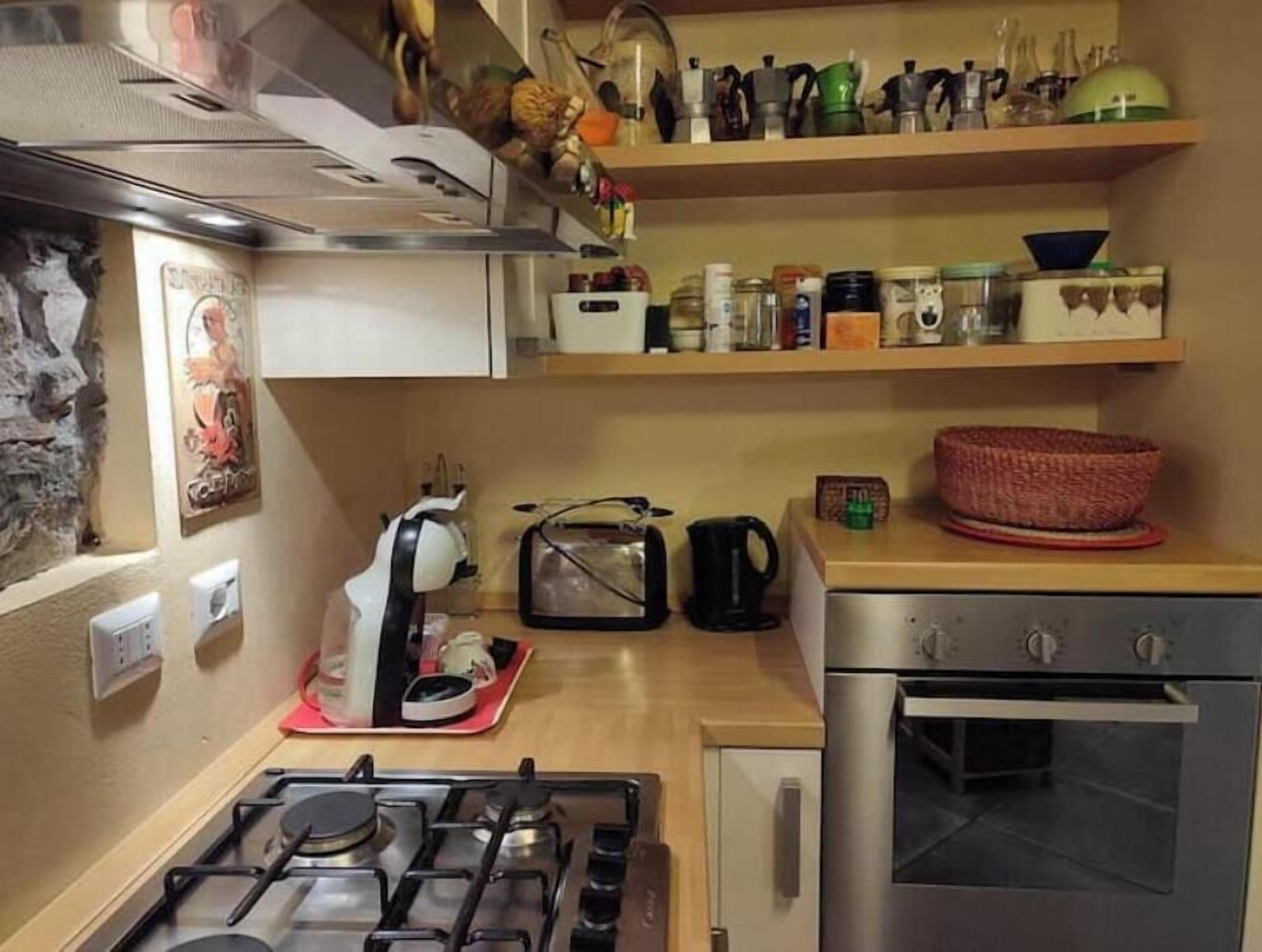 Une cuisine compacte équipée d’une cuisinière à gaz, d’un four et d’un four à micro-ondes. Des étagères au-dessus du plan de travail servent à ranger divers ustensiles de cuisine.