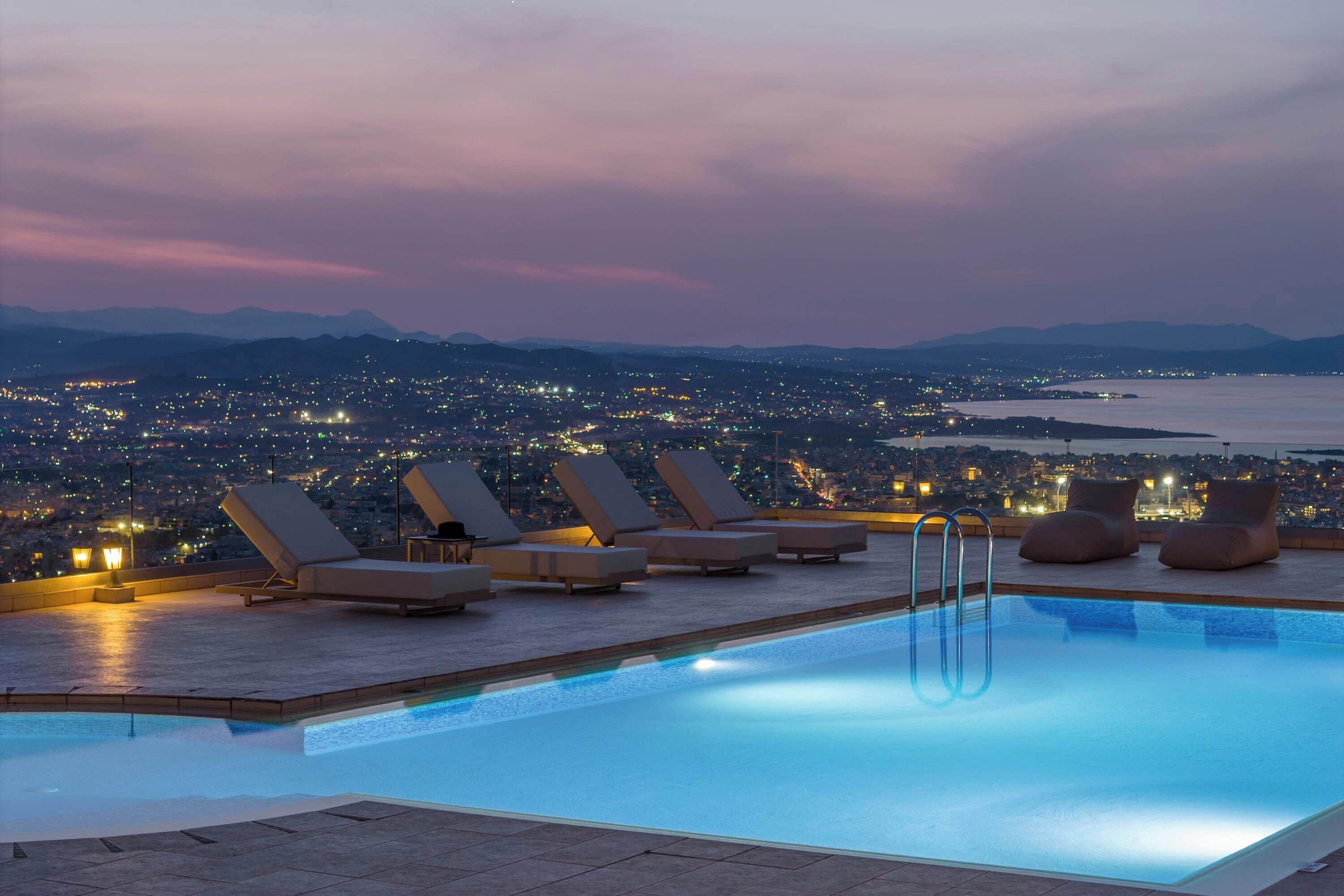 Ein Pool auf dem Dach mit Liegestühlen und Blick auf die Stadt bei Einbruch der Dunkelheit.