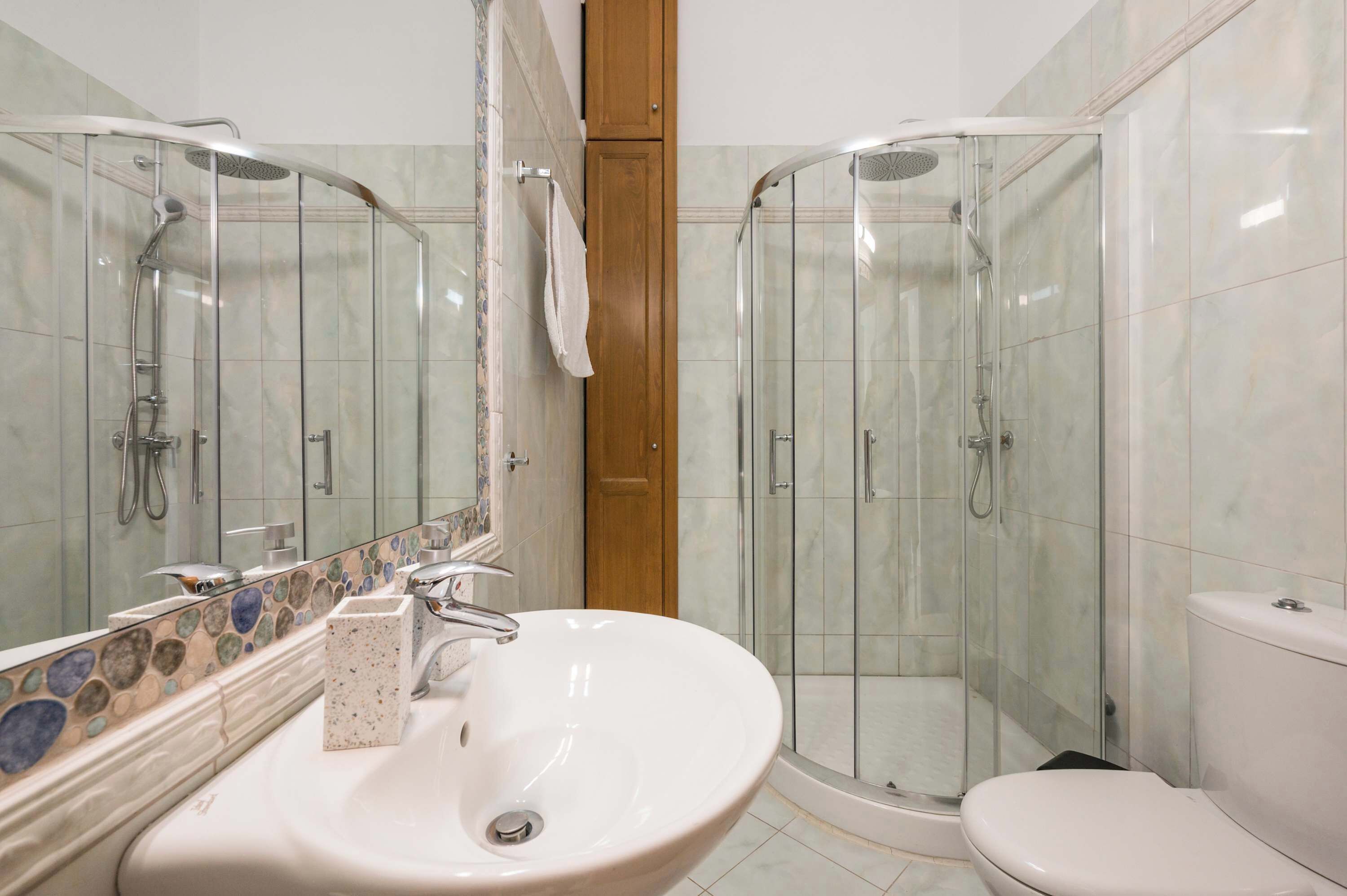 Een badkamer met een wit wastafel, een spiegel, een douche met glazen deuren en een toilet.
