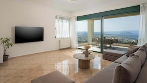 A spacious living room with a large flat-screen TV, a comfortable sofa, a round coffee table, and a view of the city through large windows. - Lithea Seaview Villa & Estate (Chania)