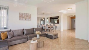 A modern living room with a sectional sofa, a coffee table, and a dining area with chairs and a table. - Lithea Seaview Villa & Estate (Chania)