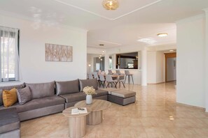 A modern living room with a sectional sofa, a coffee table, and a dining area with chairs and a table. - Lithea Seaview Villa & Estate (Chania)