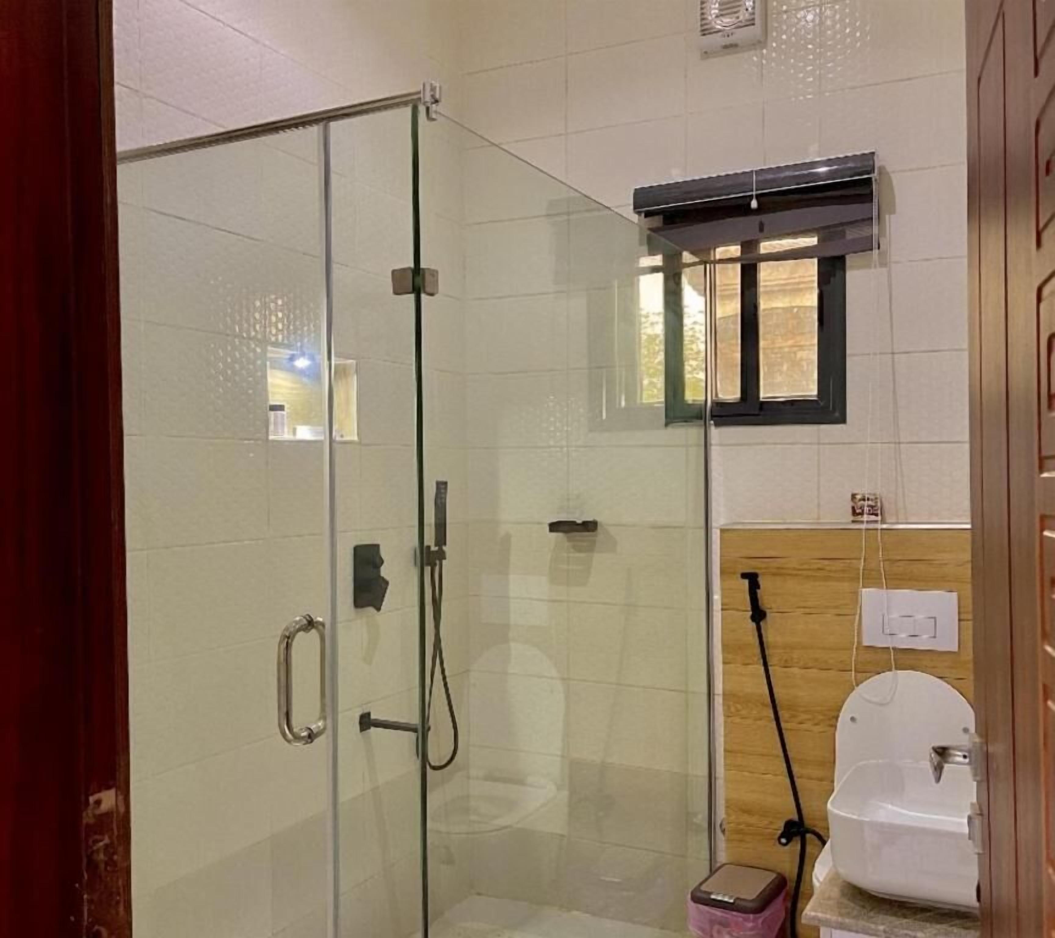 Box doccia in vetro con soffione a mano, WC con funzione bidet e finestra sopra il water.