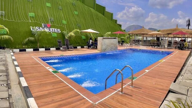 Una piscina con cubierta de madera, sillas de descanso, sombrillas y una pared con vegetación y un letrero que dice 'LISA SUITES'.