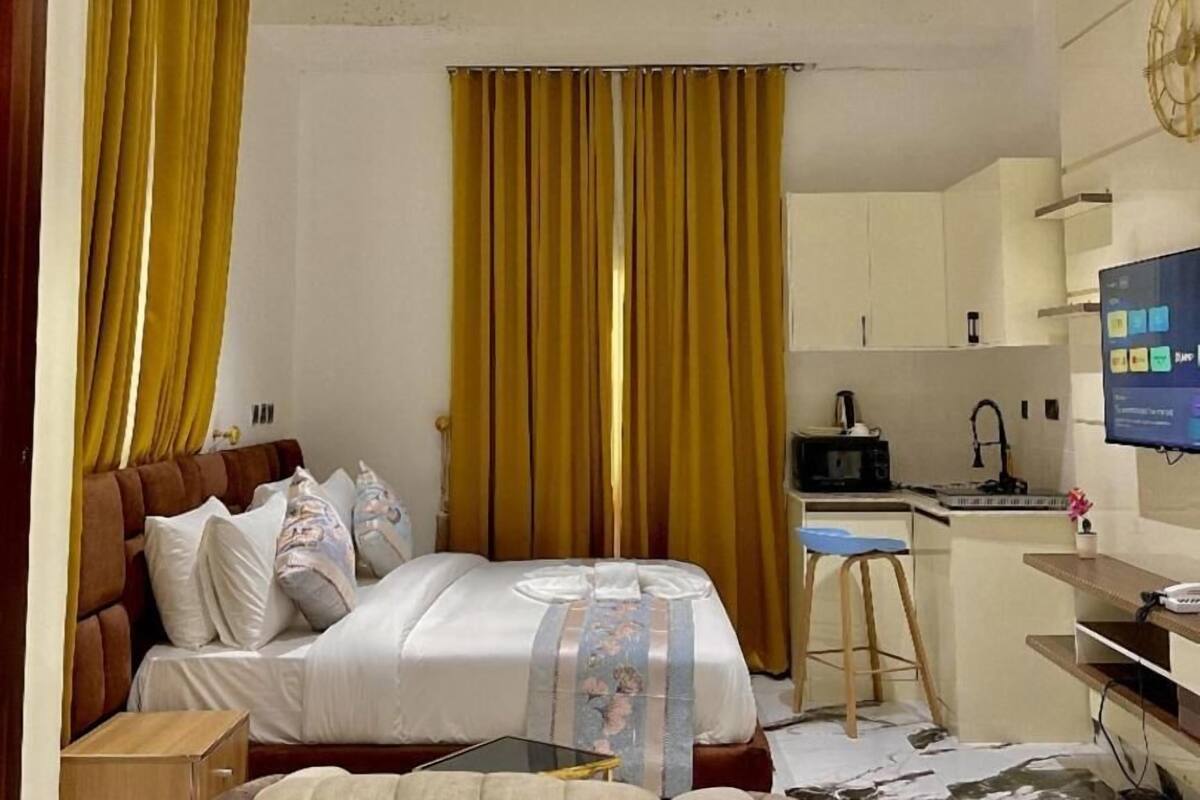 Habitación de hotel con cama, escritorio, silla, televisión y área de cocina.