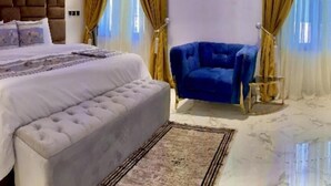 Un dormitorio con una cama grande, un sillón azul y suelo de mármol.