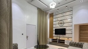 Una sala moderna con sofás capitonados, una mesa de centro redonda de vidrio, un televisor de pantalla plana montado en una pared de mármol y un mueble de madera abajo.