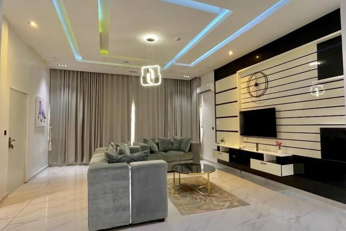 Una sala moderna con un sofá seccional, una mesa de centro, un televisor de pantalla plana y un mueble de entretenimiento fijado a la pared.