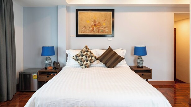 Habitación de hotel con una cama grande, dos mesitas de noche con lámparas, una obra de arte en la pared y una puerta que da a otra habitación.