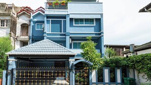 Un edificio residencial de varios pisos con fachada azul, entrada protegida por un portón y un pequeño porche cubierto.