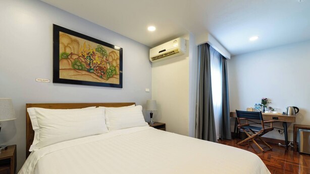 A hotel room with a large bed, a desk with a chair, an air conditioner, and a painting on the wall. - Room-handcrafted Comfort in a Lavish tra (Bangkok)