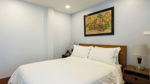 A neatly made bed with white linens, a wooden headboard, a bedside table with a lamp, and a wall-mounted painting. - Room-handcrafted Comfort in a Lavish tra (Bangkok)