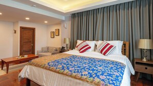 Quarto de hotel com uma cama grande, uma mesa de cabeceira de madeira, uma escrivaninha e uma cadeira.