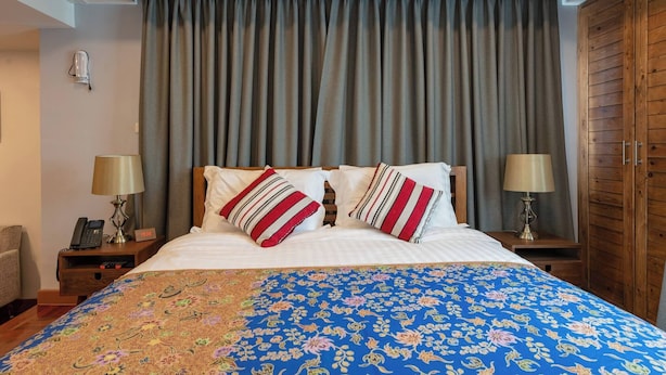 Quarto de hotel com cama, duas luminárias de cabeceira, telefone, relógio, guarda-roupa e luz de teto.
