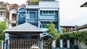 Um edifício residencial de vários andares com fachada azul, entrada com portão e um pequeno alpendre coberto.
