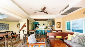 Uma sala de estar ampla com sofá, cadeiras, mesa de centro, mesa de jantar e cozinha ao fundo.