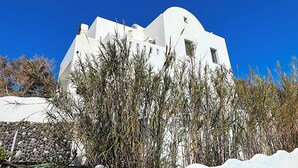 A white building with a unique architectural design, surrounded by tall grasses. - Villa Gala (Kamari)
