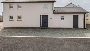 A two-story building with a flat roof, a black door, and a small attached garage. - Kiloran (Rhosneigr)