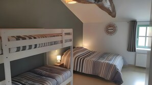 Ett rum med en våningssäng, ett sluttande tak, en vägglampa och ett fönster med gardiner.