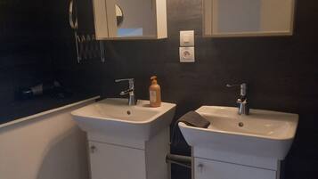 A bathroom with two sinks, a mirror, a towel rack, and a trash can.