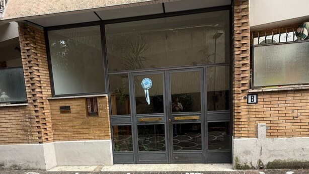 Un ingresso di un edificio con porta in vetro, pavimento in piastrelle e facciata in mattoni.