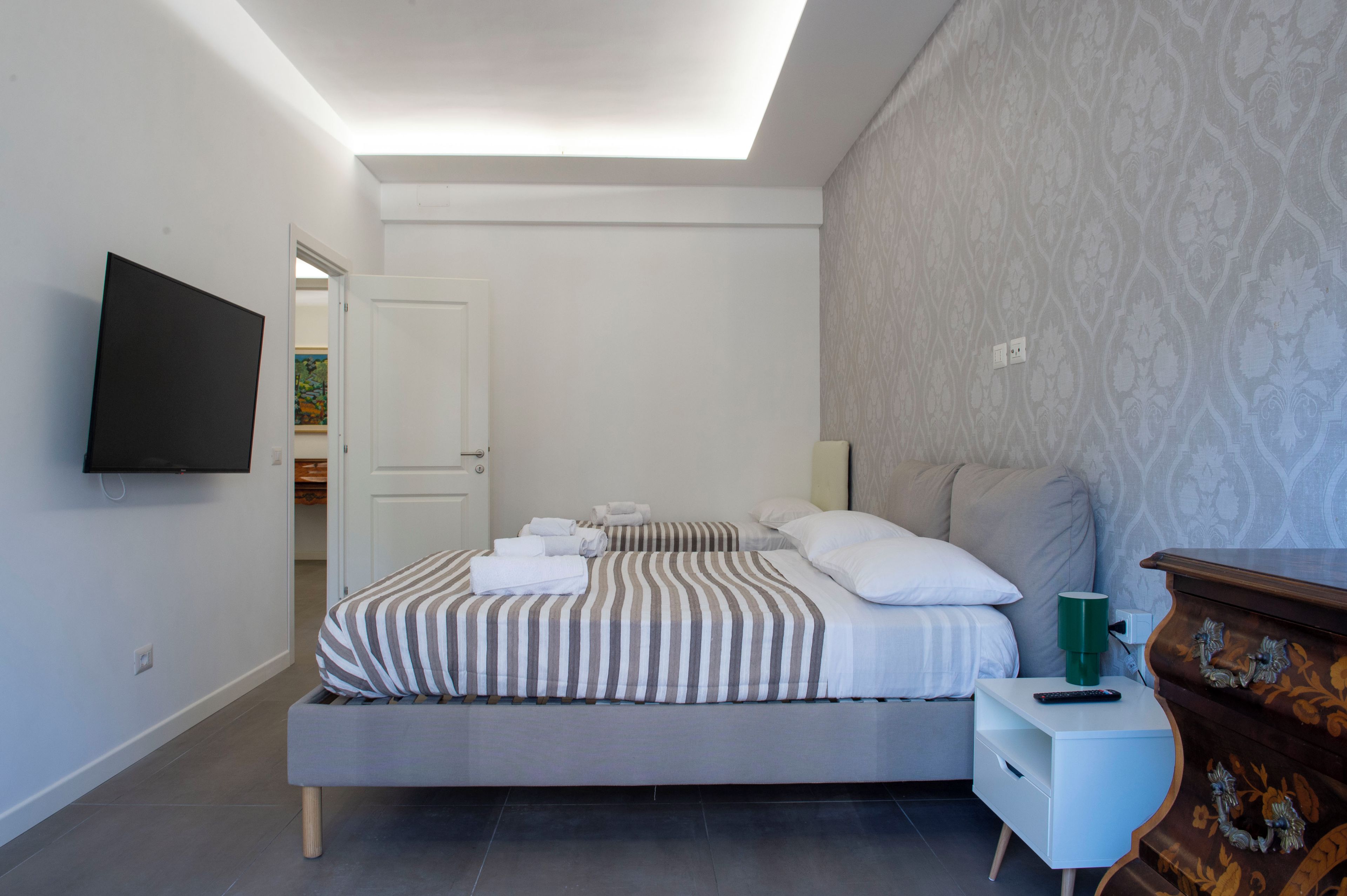 Een moderne slaapkamer met een bed, nachtkastjes, een televisie en een behang met een patroon.