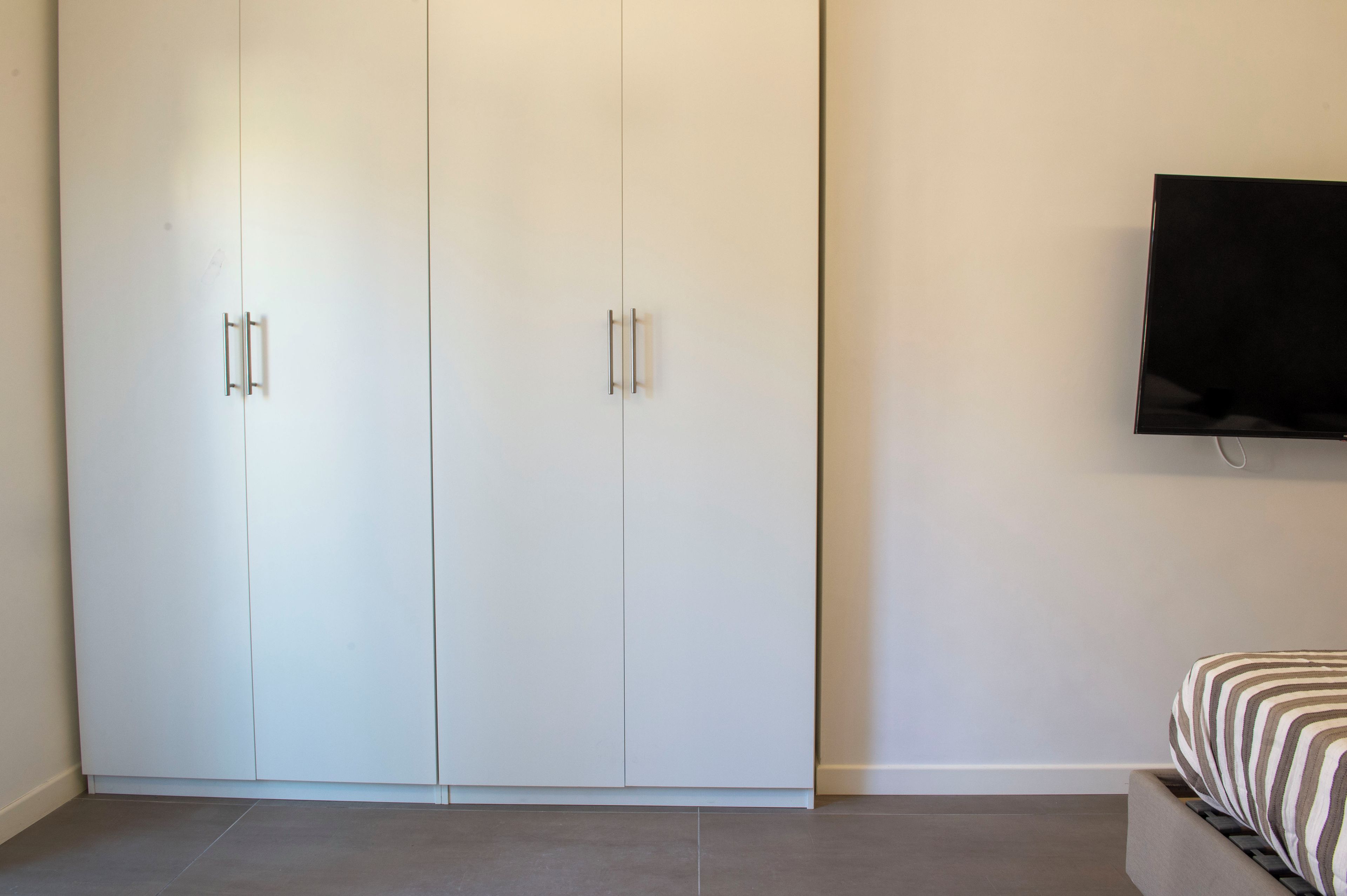 A bedroom with a bed, a wardrobe, and a television on the wall.