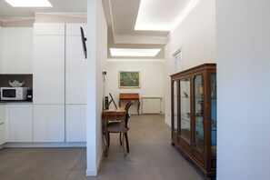 A modern kitchen with white cabinets, a microwave, and a dining area with a wooden table and chairs. - Orietta Boutique Apartment, Trastevere Station (Roma)