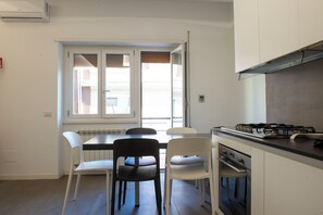 Une cuisine compacte comprenant une table et des chaises, une cuisinière à gaz et une fenêtre avec des stores.