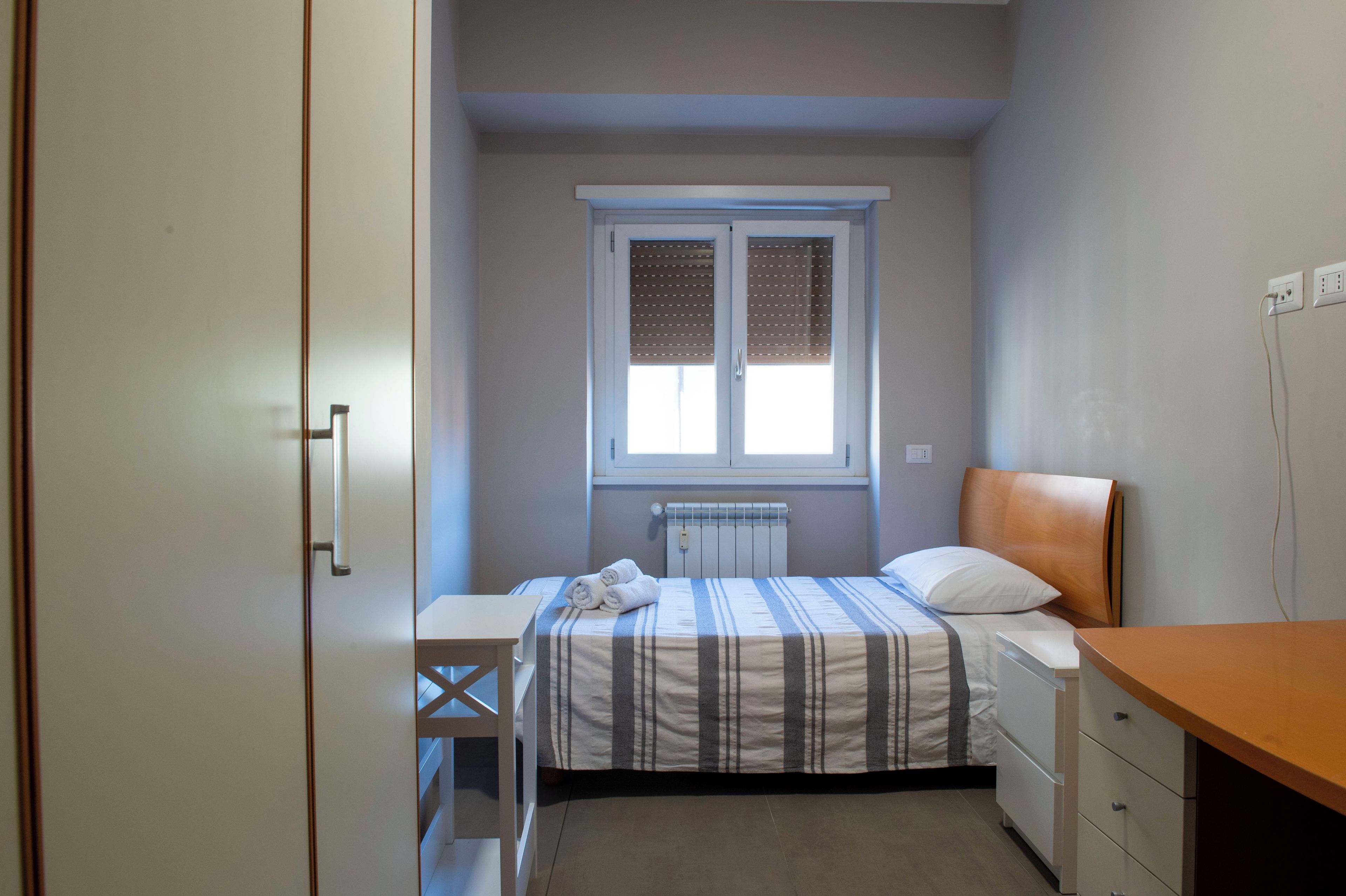Une chambre à coucher comprenant un lit, une table de chevet, un radiateur, une fenêtre avec des stores et une armoire.