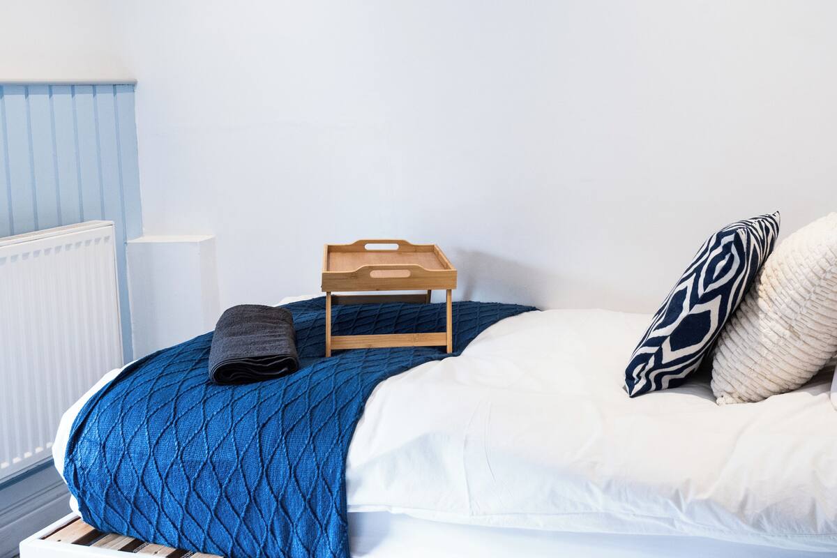 A neatly made bed with a blue quilt, white pillows, and a wooden tray.