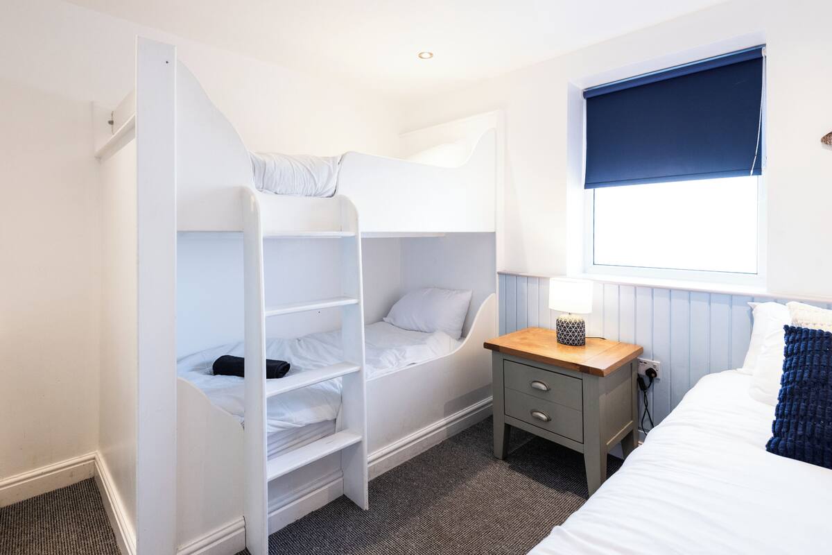 A bunk bed room with a desk and a window.