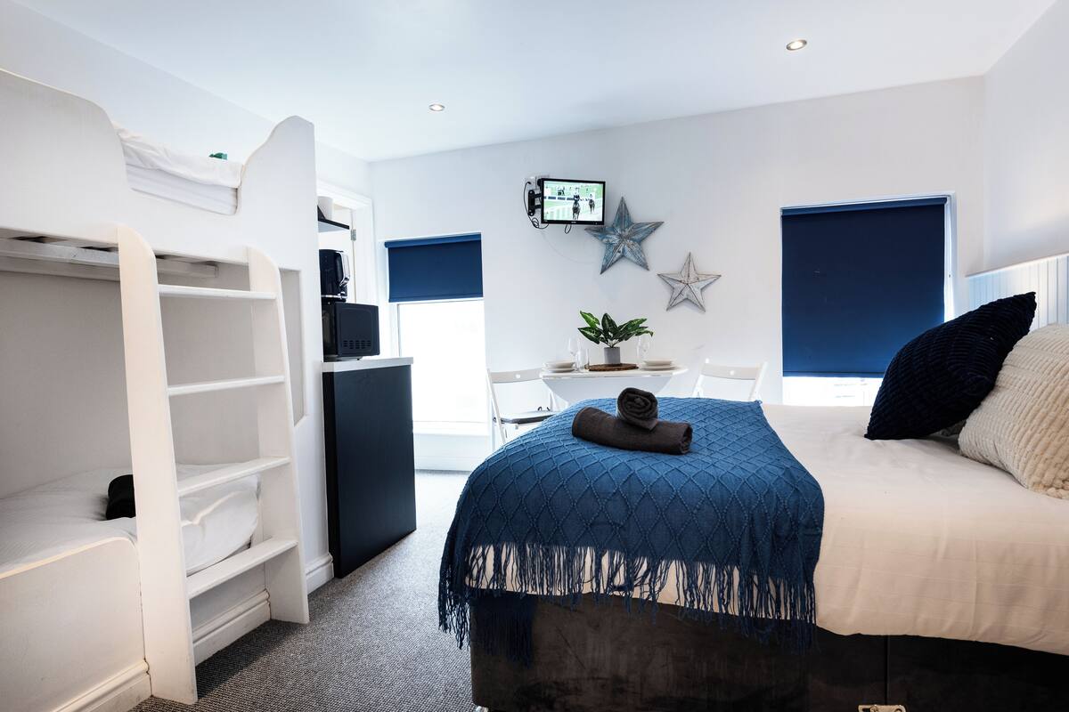 A bedroom with a bed, a desk, a chair, a TV, and a wardrobe.
