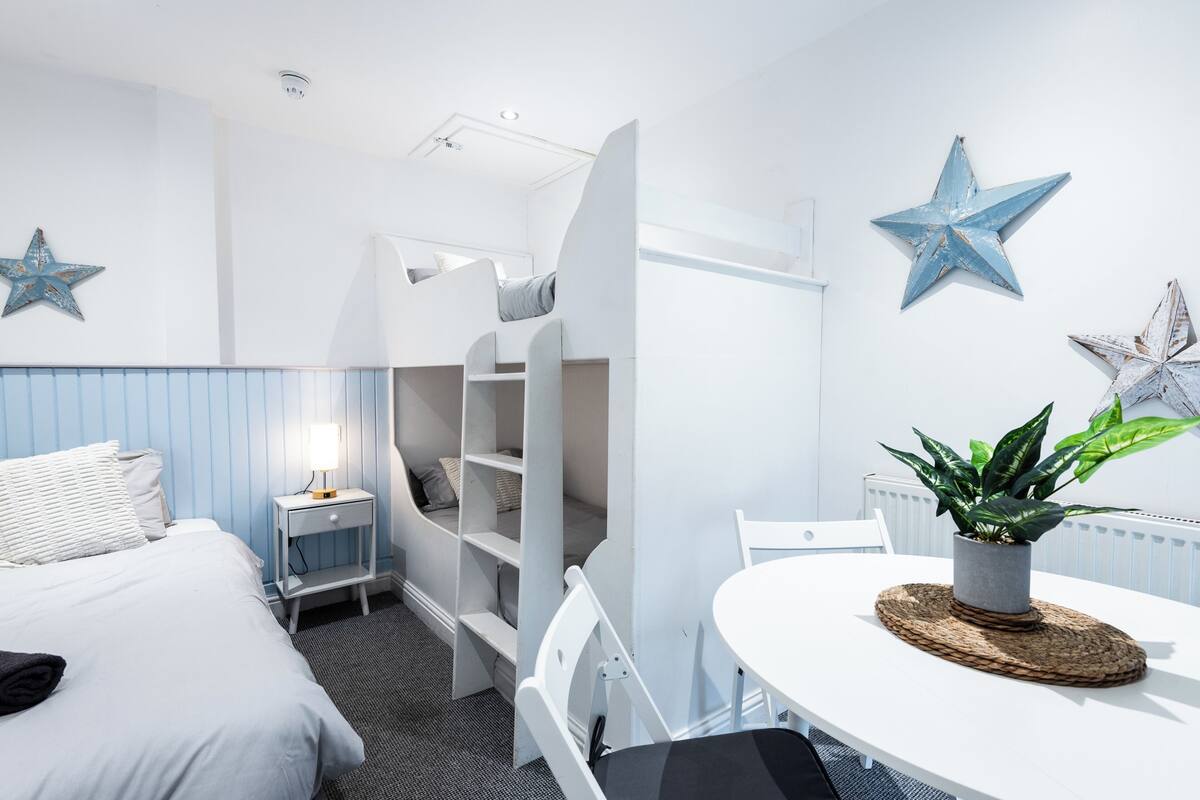 A bedroom with a bunk bed, bedside table, lamp, and decorative stars.