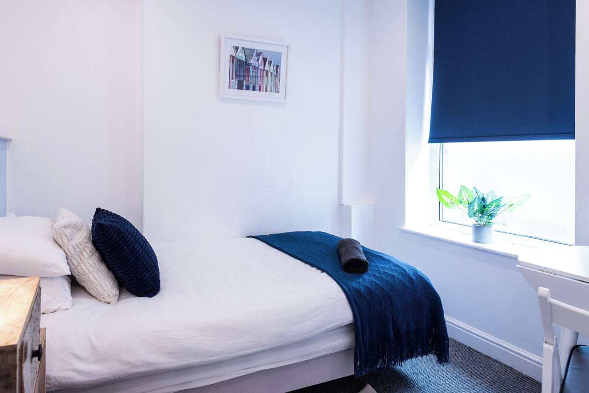 A neatly made bed with a white headboard, a bedside lamp, and a blue throw blanket.