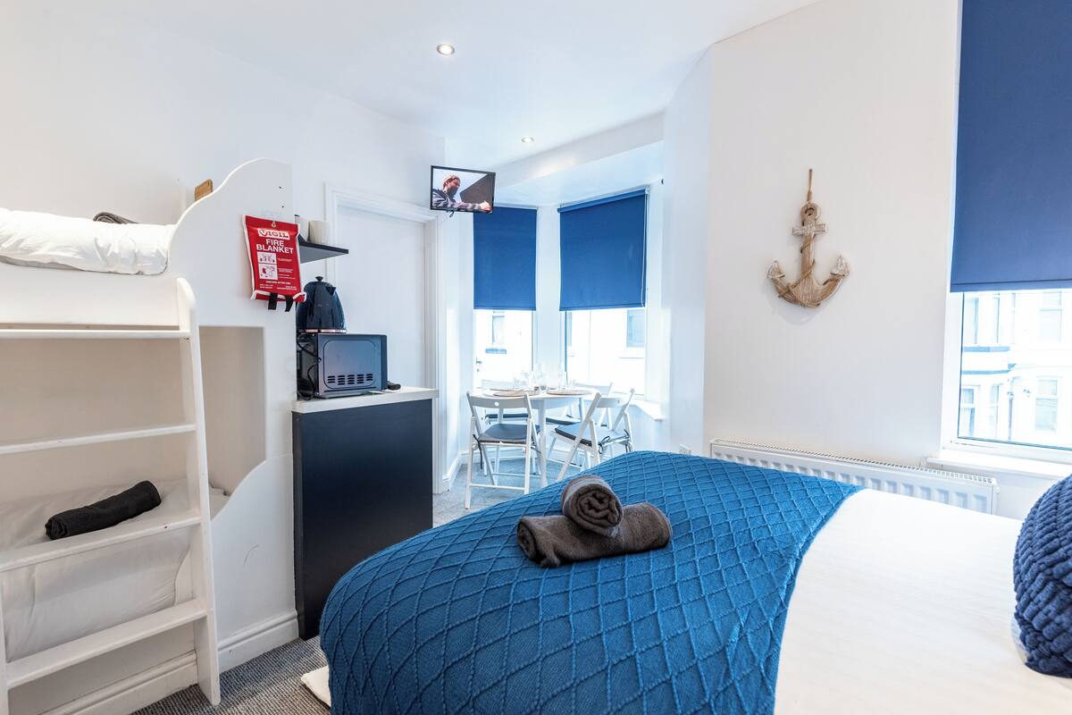 A hotel room with a bed, a desk, a chair, a TV, a fire blanket, and a window with a view.